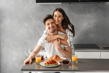 Portait of gorgeous couple looking at you and smiling, while woman hugging man during breakfast in...
