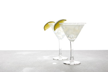 close up view of alcohol margarita cocktails with lime on grey surface on white