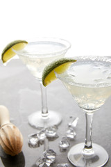 Selective focus of alcohol margarita cocktails with lime pieces and wooden squeezer on grey surface on white