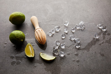 close up view of wooden squeezer, limes and ice cubes for cocktail on grey surface