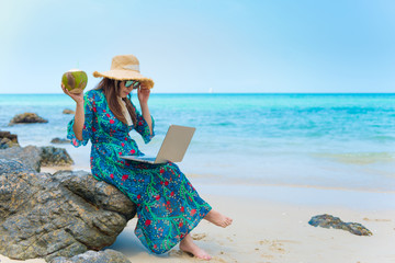 Asian woman is working while traveling on the beach during vacation summer time.