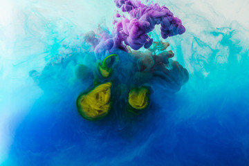 close up view of mixing of blue, turquoise, yellow and purple paints splashes  in water