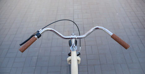 Steering wheel of a beige bicycle with brown handles on an avenue of paving slab