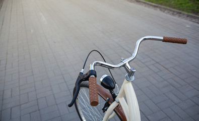 Fototapeta na wymiar Steering wheel of a beige bicycle with brown handles on an avenue of paving slab