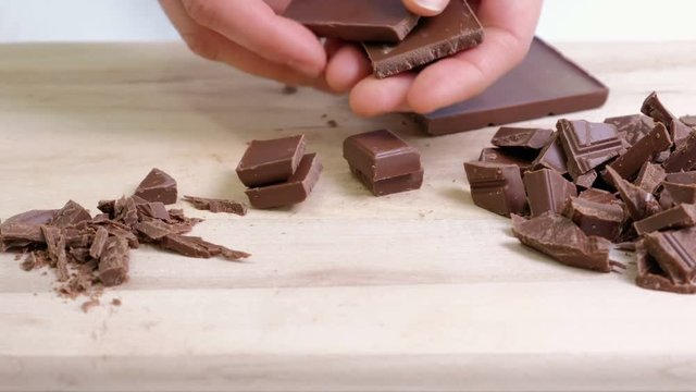 Cook hands cutting chocolate bar with a kitchen knife on cutting board.