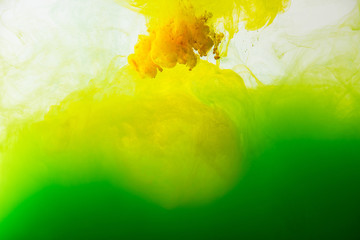 close up view of mixing of green and yellow paints splashes in water isolated on gray