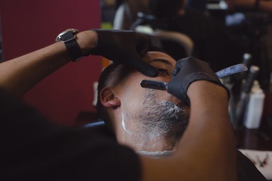 Barber shaving man's beard with straight razor in salon