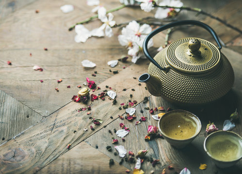 Traditional Asian tea ceremony arrangement. Iron vintahe teapot, cups, blooming almond flowers, dried rose buds and candles over wooden table background, selective focus, copy space
