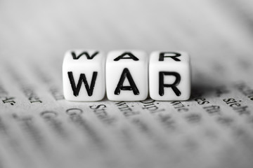 Word WAR formed by wood alphabet blocks on newspaper