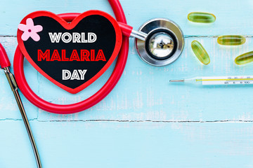 World MALARIA day April 25, Healthcare and medical concept. Stethoscope, red and black heart, thermometer and yellow Pill on blue Pastel wooden table background texture.