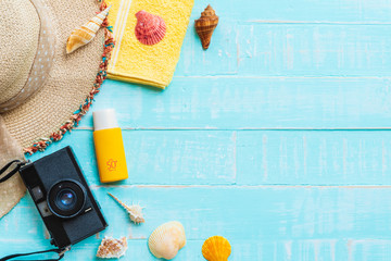 Beach accessories including sunglasses, sunscreen, hat beach, shell, yellow towel and retro camera on bright blue pastel wooden background for summer holiday and vacation concept.