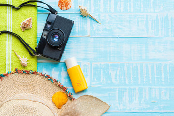 Beach accessories including sunglasses, sunscreen, hat beach, shell, green towel and retro camera on bright blue pastel wooden background for summer holiday and vacation concept.