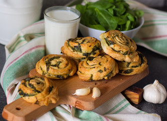 Buns of puff pastry with spinach and garlic on a wooden board in the background of a bowl of spinach and towels. Homemade pastries with greens.
