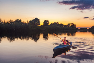 sporty man kayaking on river surrounded by forest at sunset