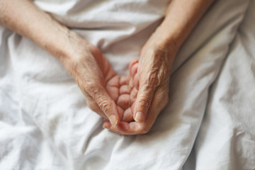 Old hands on a white background. Grandmother in bed.