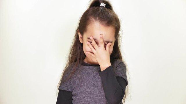 Little cute caucasian girl looking at camera, smiling, doing facepalm, showing emotion of disappointment, portrait, white background 50 fps