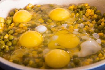 fried eggs with peas and corn on a white frying pan