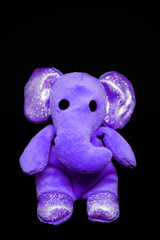 Small cute violet plush toy elephant on black background as template for greeting card with copy space for text or message at the top.
