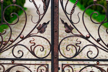 A closed forged metal gate looking onto a garden path
