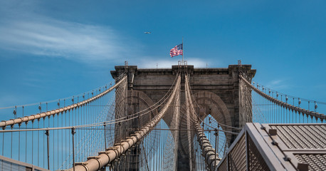 Brooklyn Bridge, New York, Manhattan with US flag and airplane at blue sky. panorama