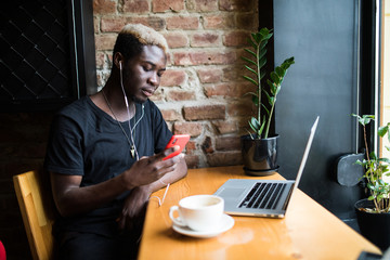 Handsome afro american man sitting at cafe , listening music and looking at phone screen