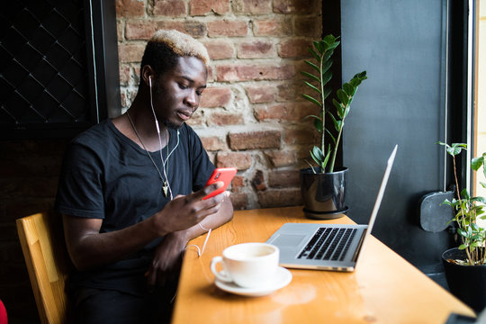 Handsome afro american man sitting at cafe , listening music and looking at phone screen