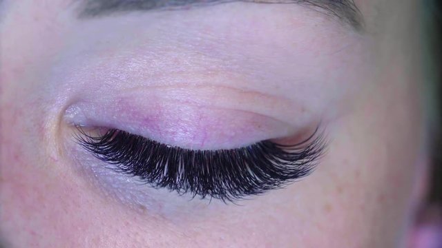Extreme close up woman eye. Eyelash extension procedure. Cosmetologist combing eyelashes with a brush