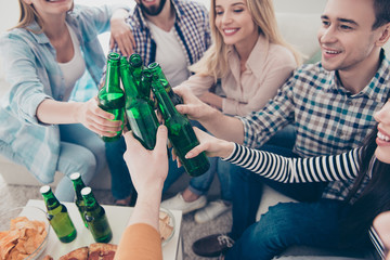Cropped close up portrait of cheerful, stylish, attractive, positive community sitting in livingroom, house having snacks on the table clinking green bottles with lager