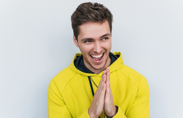 Studio closeup shot of sneaky sly and scheming young European man dressed in stylish yellow hoodie  looking at camera with mysterious smiles, male making gesture as if washing his hands. Body language - obrazy, fototapety, plakaty