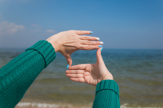 Closeup of female caucasian hands isolated on blue background. Young woman forming frame with her two hands as if looking at something virtual and invisible in sea.
