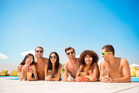 Six friendly multi ethnic hot teens in diverse swim wear and spectacles are chatting in the pool, sunshine, blue sky, chill, drinks are on white wooden floor, holiday together