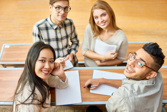 High angle view at multi-ethnic group of cheerful students looking at camera and smiling sitting at desk in lecture hall of modern college