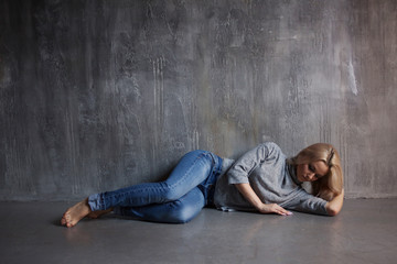 Sad woman lying on the floor. Depression and chronic fatigue. Young beautiful blonde in a gray...