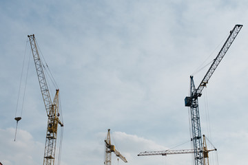 Industrial construction cranes and building silhouettes over sun at sunrise.