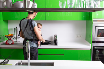 Young man making breakfast with his baby in carrier