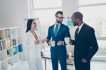 Fototapeta premium Three stylish, modern, cheerful partners in tux, tuxedo having break time, speaking during coffee time, standing in work place, station, holding mug with coffee in hands, men with bristle, in glasses