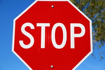 Stop Sign Close Up with Trees Frame Right and Clear Blue Sky in the Background
