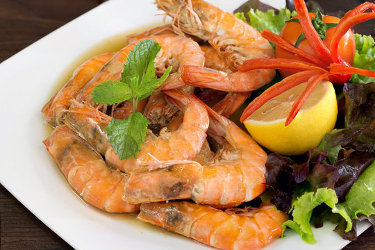 Bake shrimp with salt in white dish which has fresh vegetables decorated on dish / Select focus.