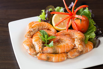 Bake shrimp with salt in white dish which has fresh vegetables decorated on dish / Select focus..