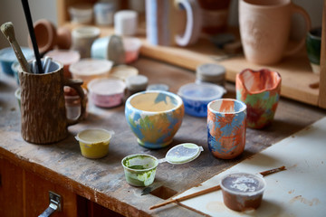 Close-up of various paint mugs and brushes in holder on worktop, selective focus, side view.
