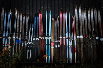 Obraz premium Red, blue, violet, black old ski made of wooden material with antique texture and grunge surface lean against the wooden dark wall of the house in northern Finland in Lapland in gloomy atmosphere