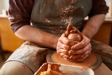 Close-up hands of a male potter in apron making a vase from clay, selective focus