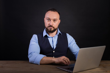 Portrait of a confident businessman with laptop computer. Confident business expert. Young handsome man in shirt and waistcoat holding a laptop and smiling while standing against. Black background