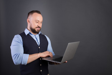 Portrait of a confident businessman with laptop computer. Confident business expert. Young handsome man in shirt and waistcoat holding a laptop and smiling while standing against. Black background