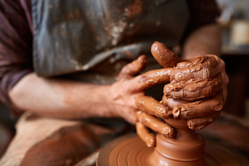 Fototapeta na wymiar A male potter in apron molds bowl from clay, selective focus, close-up