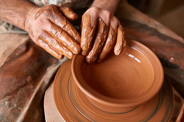 Close-up hands of a male potter in apron molds bowl from clay, selective focus