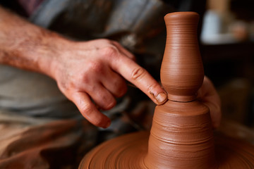 A male potter in apron molds bowl from clay, selective focus, close-up