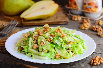 Quick pear and cabbage salad. Homemade salad with fresh pear, cabbage and walnuts on a white plate and on rustic wooden background. Quick healthy salad idea. Closeup