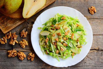 Easy pear and cabbage salad. Home salad with fresh raw pear, cabbage and walnuts on a white plate and on rustic wooden background. Healthy vegetarian salad recipe. Top view