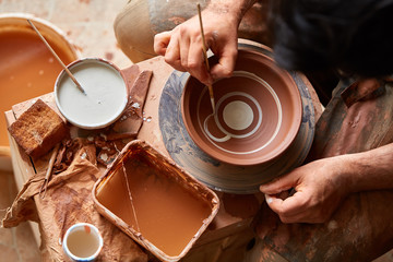 A potter paints a clay plate in a white in the workshop, top view, close-up, selective focus.